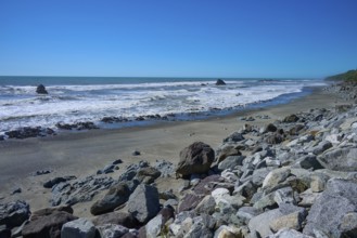 Rocks spread along a sunny sandy beach with waves in the background, West Coast, South Island, New