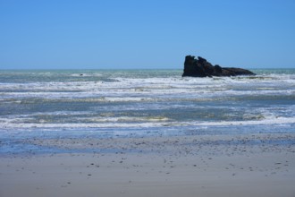 The picture shows a beach with rocks and gentle waves under a clear blue sky, West Coast, South
