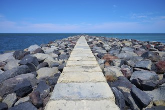 A stony path leads into the sea, surrounded by a sunny coastal landscape, Mana Bay, Patea,