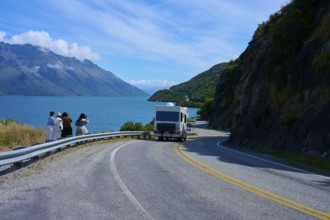 People enjoying travelling and a motorhome on a winding road next to a lake surrounded by