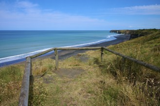 Viewing platform with wooden railing overlooks black sand beach and cliffs on a quiet coast, Mana