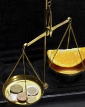 Historic scales with euro money and a piece of an orange in dark back