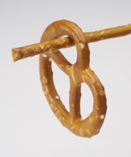 Small lye pretzel hanging on a salt stick in light back