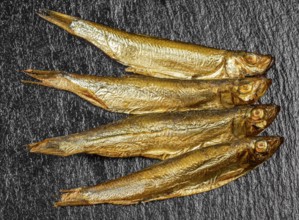 Arrangement with fresh smoked sprats on dark stone slab
