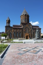 A red church with classical architecture and a stone monument under a clear sky, Church of the Holy
