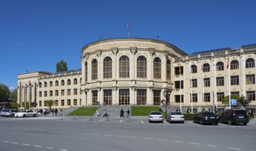 A large classical building with flags, cars and people under a clear sky, Gyumri, Gyumri, Gyumri,