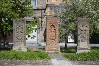 Three artistically engraved khachkars stand in a green setting, cross stones, khachkars, Gyumri,