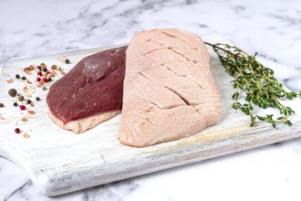 Fresh raw duck breasts, spread on a wooden cutting board, with herbs and spices, on a white marble