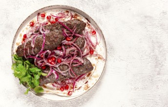 Grilled kebabs topped with onions and pomegranate on a white plate in a bright kitchen setting