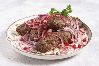 Grilled kebabs topped with onions and pomegranate on a white plate in a bright kitchen setting