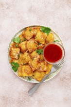 Fried ravioli with parmesan cheese, served with red sauce and garnished with herbs, on a light