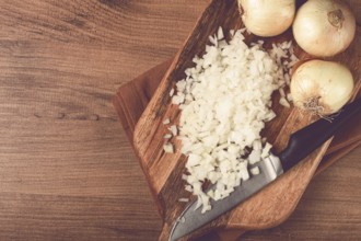 Finely chopped onion on a chopping board with a knife, wooden table, top view, no people