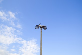 Motorcycle on the pedestal. A light motorbike on a pole, put up as a dummy or a monument.