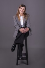 Elegant senior businesswoman sitting on a stool and smiling at the camera