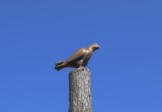 Figurine of a falcon on a stump of a tree against the blue sky. Taman, Krasnodar Krai, Russia