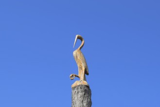 Figure of crane on the stump of a tree against the blue sky. Taman, Krasnodar Krai, Russia