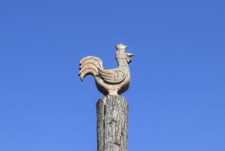 Figurine of a rooster on a tree stump on a background of blue sky. Taman, Krasnodar Krai, Russia