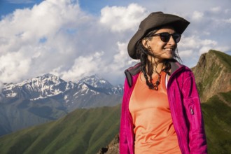 Happy Young Traveler hiker woman portrait wearing hat and jacket smiling in Kazbegi National Park