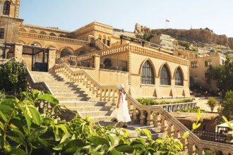 Traveler woman in white dress walking stairs of historic building - visit Mardin museum in old city