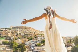 Traveler woman in white dress arms outstretched looking over panoramic view of historic city of
