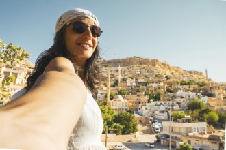 Smiling woman in sunglasses taking selfie with panoramic skyline of historic Mardin Turkey and