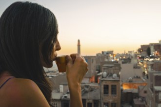 Tourist woman enjoying traditional Mirra coffee on rooftop with Mardin skyline and Mesopotamian