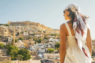 Traveler woman in white dress looking over panoramic view of historic city of Mardin Turkey with