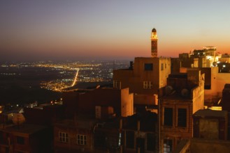 Illuminated mosque minaret above Mardin old town with glowing city lights and Mesopotamian plains