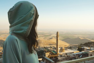 Smiling woman traveler in abaya standing above Mardin Turkey with panoramic view of Mesopotamian