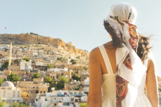 Traveler woman in white dress looking over panoramic view of historic city of Mardin Turkey with