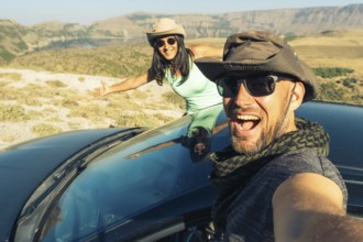 Happy young caucasian couple taking selfie while sitting in rented vehicle black car having road