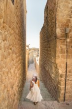 Traveler woman in white dress walking through narrow stone alley in historic city of Mardin Turkey
