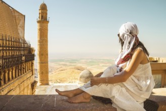 Traveler woman in white dress sitting near Great Mosque of Mardin Ulu Camii with panoramic view of