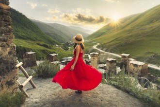 Woman in red dress looking at medieval towers of Ushguli Georgia during sunset with mountains and