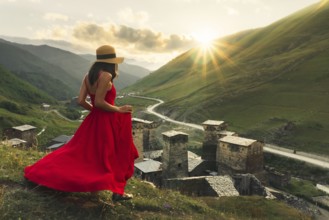 Woman in red dress looking at medieval towers of Ushguli Georgia during sunset with mountains and