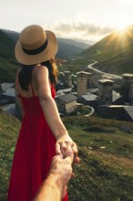 Young Couple holding hands leading way in Ushguli Georgia woman in red dress leading towards
