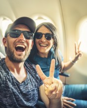 Happy casual dressed tourist taking selfie inside airplane - Cheerful couple on summer vacation -