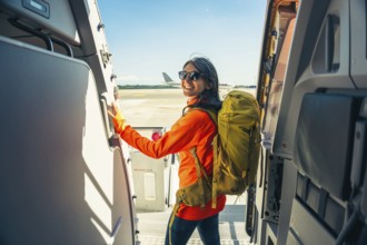 Young happy caucasian female traveler backpacker with carry on hiking backpack boarding airplane
