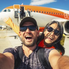 Happy couple of tourists boarding outside to plane at the airport - Happy man and woman having