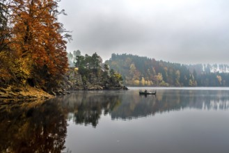 Foggy Landscape With Fishermans Boat On Calm Lake And Autumnal Forest At Lake Ottenstein In Austria