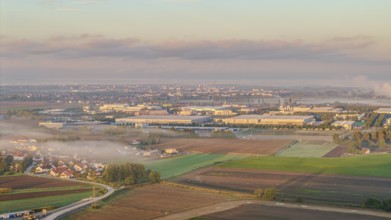 An extensive industrial area becomes visible in the morning sun. Fog envelops the landscape and the