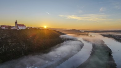 The sun rises over the Danube while mist drifts over the water. A tranquil landscape with trees and