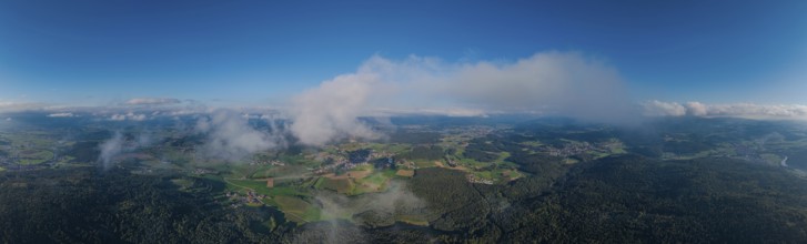 The photo shows a wide landscape with rolling hills and forests under a clear, blue sky. The sun is