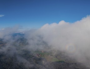 A far-reaching view of Germany's green landscape, surrounded by clouds. The sky is blue and clear.