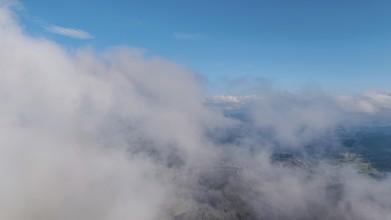 Wide clouds drift over a sunny landscape. Flat hills and part of the village are visible in the