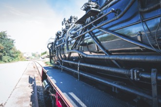 Partial view of a shiny steam locomotive showing the detailed mechanics and the railway landscape,