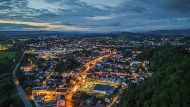A quiet town in Germany appears at dusk. Lights from the streets glow softly while the surrounding