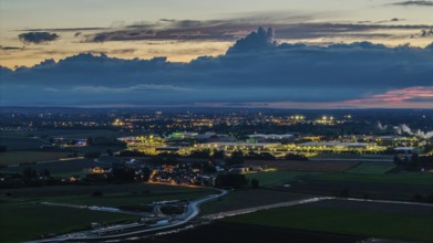 The scene shows an expansive landscape at dusk. Illuminated buildings and streets are visible in