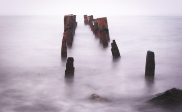 Wooden bridge remains in silky water with sea horizon in the background. Concept of time and