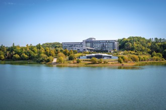 Organic lakeside hotel surrounded by trees under a clear blue sky, Zeulenrodaer Meer reservoir,
